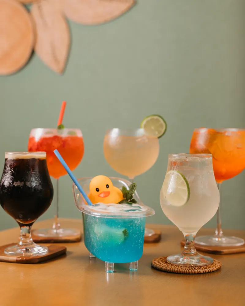 Drinks coloridos em taças sobre a mesa, com um copo azul decorado com patinho amarelo