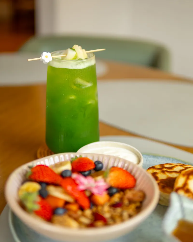 Suco verde com florzinha e tigela de frutas frescas sobre a mesa