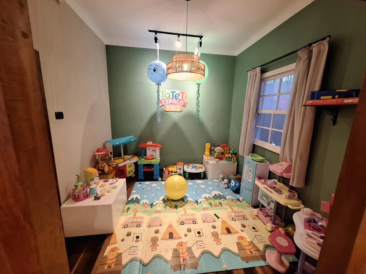 Espaço Kids do Momentos: sala de paredes verdes com tapete colorido, prateleiras e muitos brinquedos